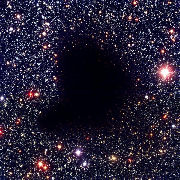Stark black blob fanning up and to the right in a dense, colorful starfield.