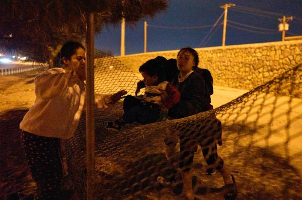 A child is passed over a chain l<em></em>ink fence after migrants made their way across the southern border.