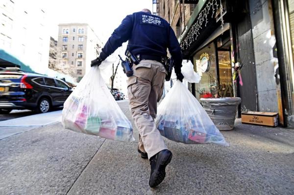 An officer walks down the street with evidence bags in both hands.