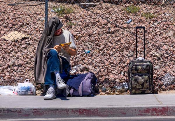 Homeless man sitting on a sidewalk in Las Vegas, checking informatio<em></em>nal paper a<em></em>bout local cooling services during a severe heatwave.