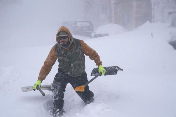 Travis Sanchez trudges over a snowdrift with a pair of shovels for a stranded motorist on Chenango Street in Buffalo, N.Y. on Saturday, Dec. 24, 2022.
