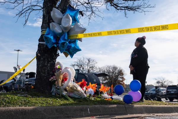 A person stands by a memorial to the Walmart victims, set up at a tree with balloons