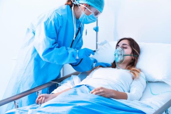 Doctor examining female patient in critical health co<em></em>nditions using a stethoscope in the intensive care unit of a modern hospital during covid-19 pandemic