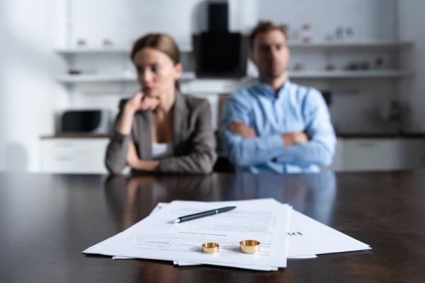 An unhappy couple sitting at a table with divorce docu<em></em>ments and their wedding bands.