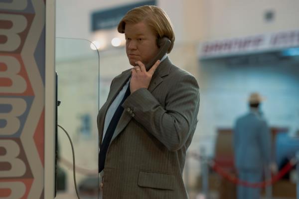 Jesse Plemons talking on a pay phone wearing a suit. 