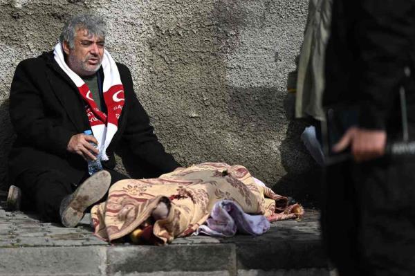 A man sits next to a body amid the rubble of buildings in Kahramanmaras, Turkey. 