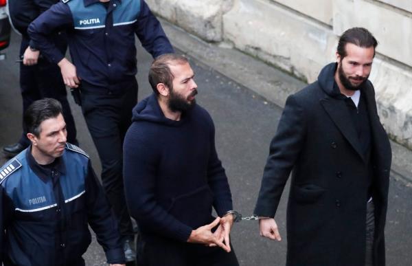 Andrew Tate making hand symbol while handcuffed to his brother Tristan as they arrived at court in Romania on Monday.