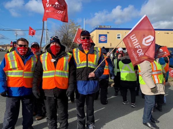 A group of people wearing coats and co<em></em>nstruction vests wave red flags that say UNIFOR on them